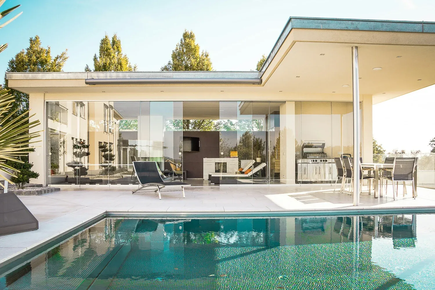 Modern house with glass walls, patio furniture, and swimming pool.